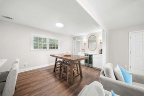 A dining area with a wooden table and chairs, a kitchen in the background, and a white door. - GSU Getaway, 4BR3BA, spacious pet friendly (Statesboro)