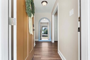 A hallway with wooden flooring, a door with a green wreath, and an arched doorway leading to an outdoor area. - GSU Getaway, 4BR3BA, spacious pet friendly (Statesboro)