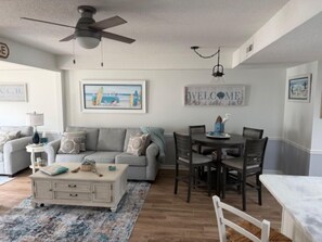 A living room with a sofa, coffee table, and dining area with chairs and a table. - Calm & Cozy Escape with Scenic Views (Surfside Beach)