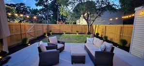 A backyard with a wooden fence, outdoor furniture, and string lights.