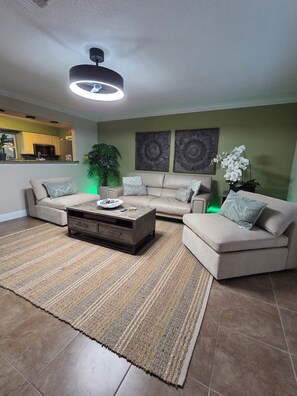A living room with a sofa set, a coffee table, a large plant, and artwork on the wall. - Cozy and convenient 2-bedroom house with pool in serene Lehigh Acres (Lehigh Acres)