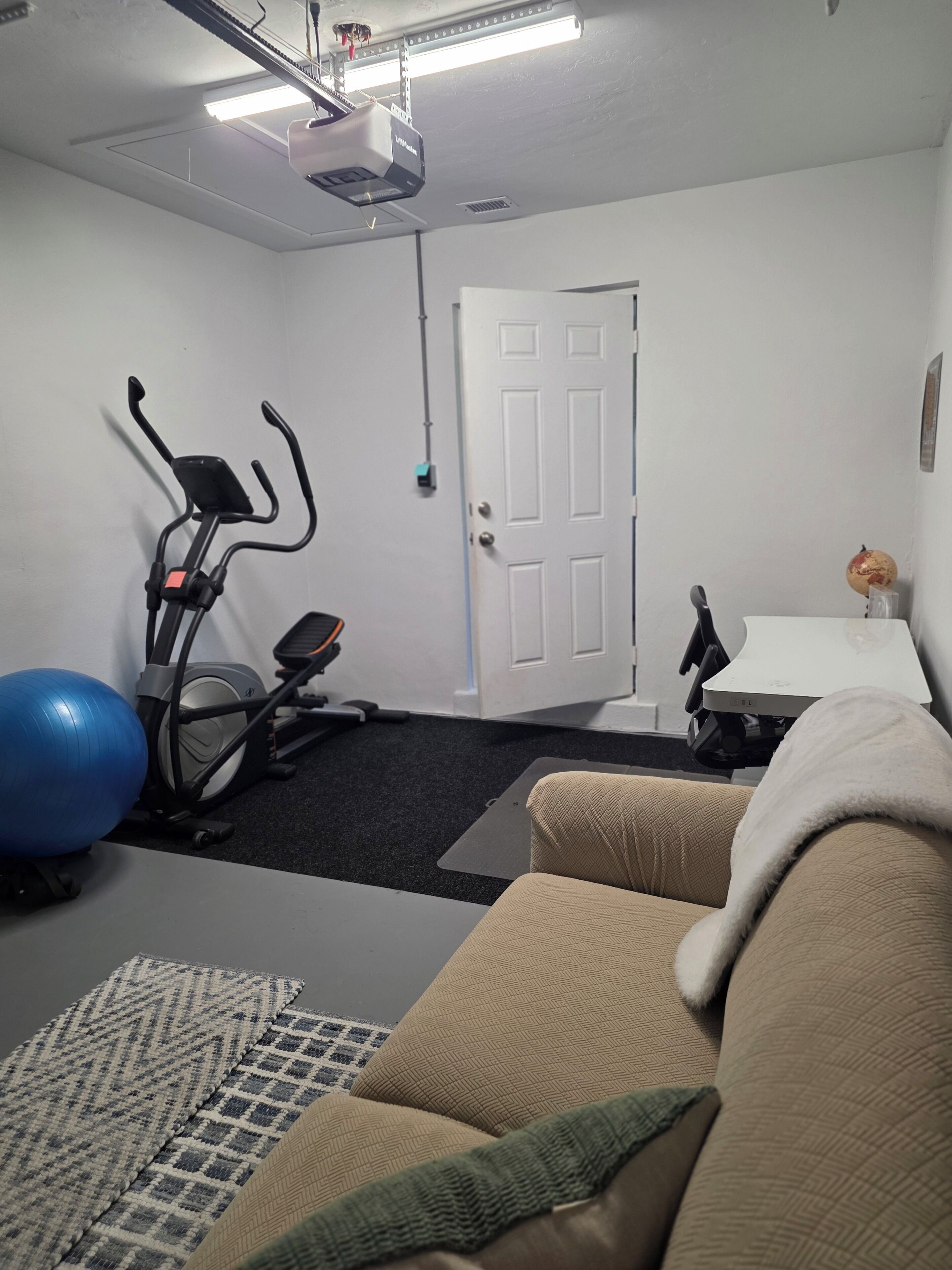 A room with a treadmill, exercise ball, and a couch.