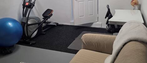 A room with a treadmill, exercise ball, and a couch.