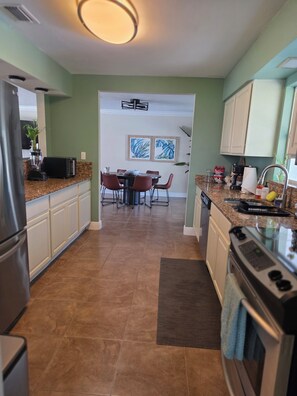 Een moderne keuken met granieten aanrechtbladen, een eethoek met een tafel en stoelen, en een doorkijk naar de woonkamer.