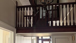 Un escalier avec une rampe en bois menant à un niveau supérieur, un lustre, une lampe et une boîte posée sur le sol.