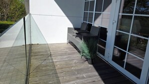 Un espace extérieur abrité doté d’une terrasse en bois, d’une véranda en verre et d’un coin salon avec des meubles en osier.