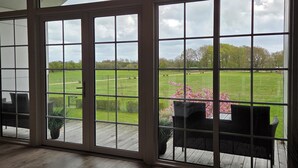 Ein Zimmer mit großen Fenstern, einer Holzterrasse und Gartenmöbeln.