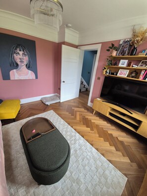 A living room with a herringbone floor, a television on a wooden stand, a painting on the wall, and a staircase leading to another room. - Fabulous 4-bedroom family home in tranquil Dublin neighborhood 10 mins from town (Dublin)