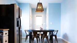 Une cuisine avec un réfrigérateur noir, une table à manger avec quatre chaises et un luminaire suspendu.