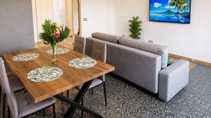 A modern living room with a wooden dining table, grey sofa, and a TV on the wall. - T3 6 pers - Sea view - Beach 1 min away - Terrace - WiFi fibre 1Gb - PortAventura (Salou)