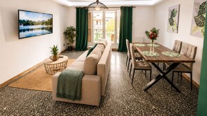 A modern living room with a sofa, dining table, and chairs. There is a large window with curtains, a hanging light fixture, and a painting on the wall. - T3 6 pers - Sea view - Beach 1 min away - Terrace - WiFi fibre 1Gb - PortAventura (Salou)