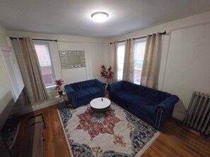 Una sala de estar con dos sofás azules, un tapete estampado, una mesa de centro redonda y un espejo decorativo en la pared.