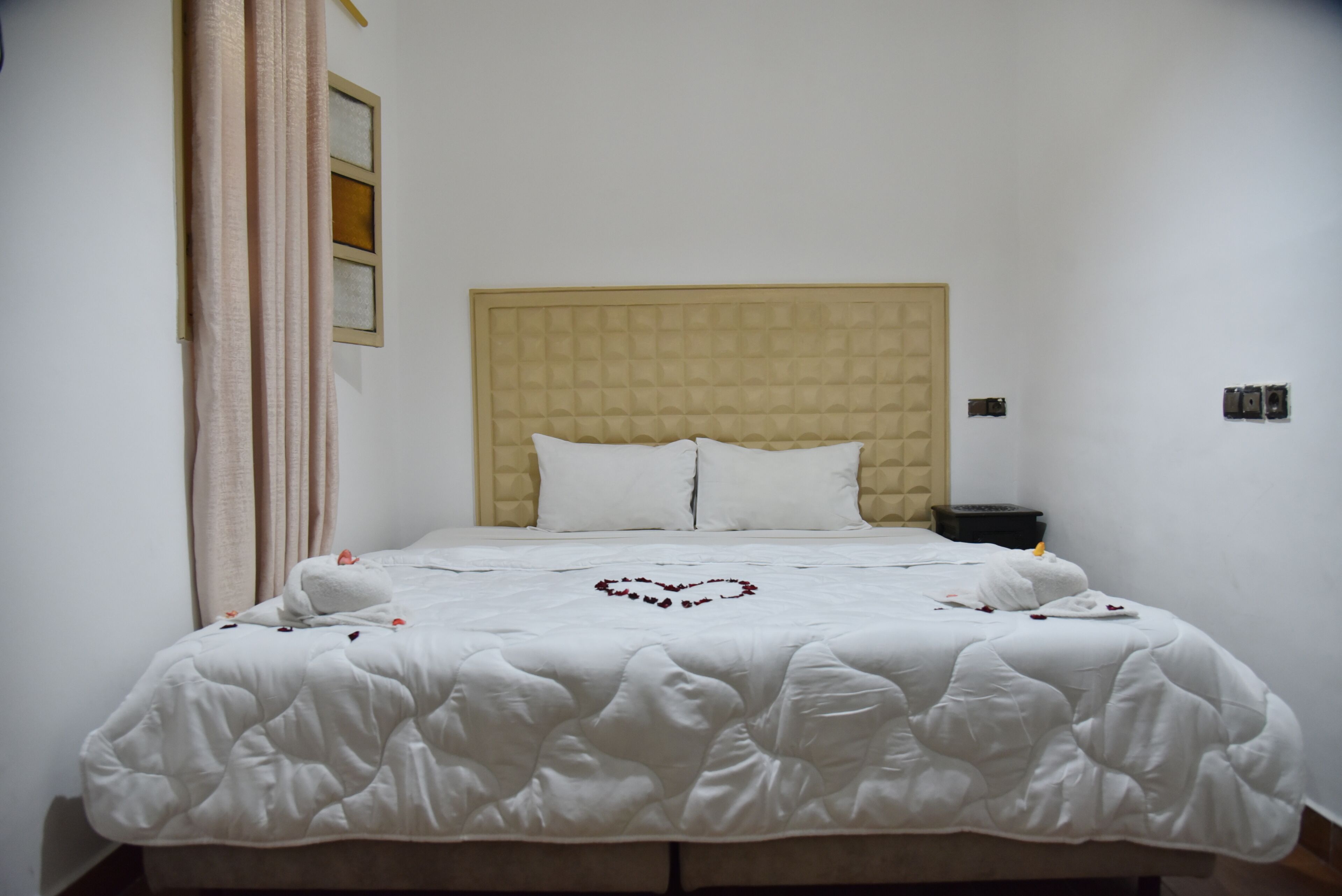 A neatly made bed with a heart-shaped decoration, a headboard, and a bedside table with a lamp.