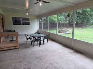 A room with a round table and chairs, a ceiling fan, and large windows offering a view of the outdoors.