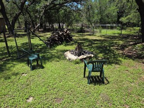 A grassy outdoor area with two green chairs, a fire pit, and a pile of logs. - Spacious 4-bedroom house in San Antonio close to many SA attractions (San Antonio)