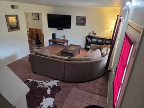 A living room with a sectional sofa, a flat-screen TV, a wooden coffee table, and a small side table.