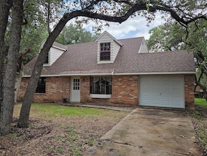 A two-story brick house with a garage, a front porch, and a large tree in front.