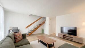 Una sala de estar moderna con una escalera, un sofá, una mesa de centro y un televisor.