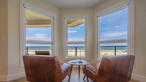 Une chambre avec vue sur la plage, deux fauteuils en cuir, une petite table et une fenêtre donnant sur l’océan.