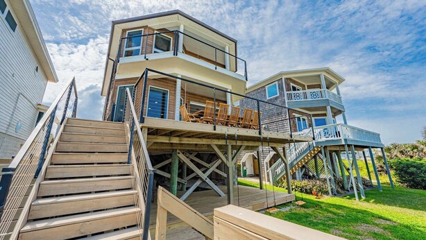 Il s’agit d’une propriété en bord de mer à plusieurs niveaux, dotée d’une terrasse en bois, d’un espace salon extérieur et d’une zone couverte offrant une vue sur l’eau.