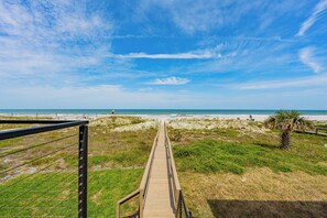 Ein hölzerner Steg führt zu einem Strand unter blauem Himmel.