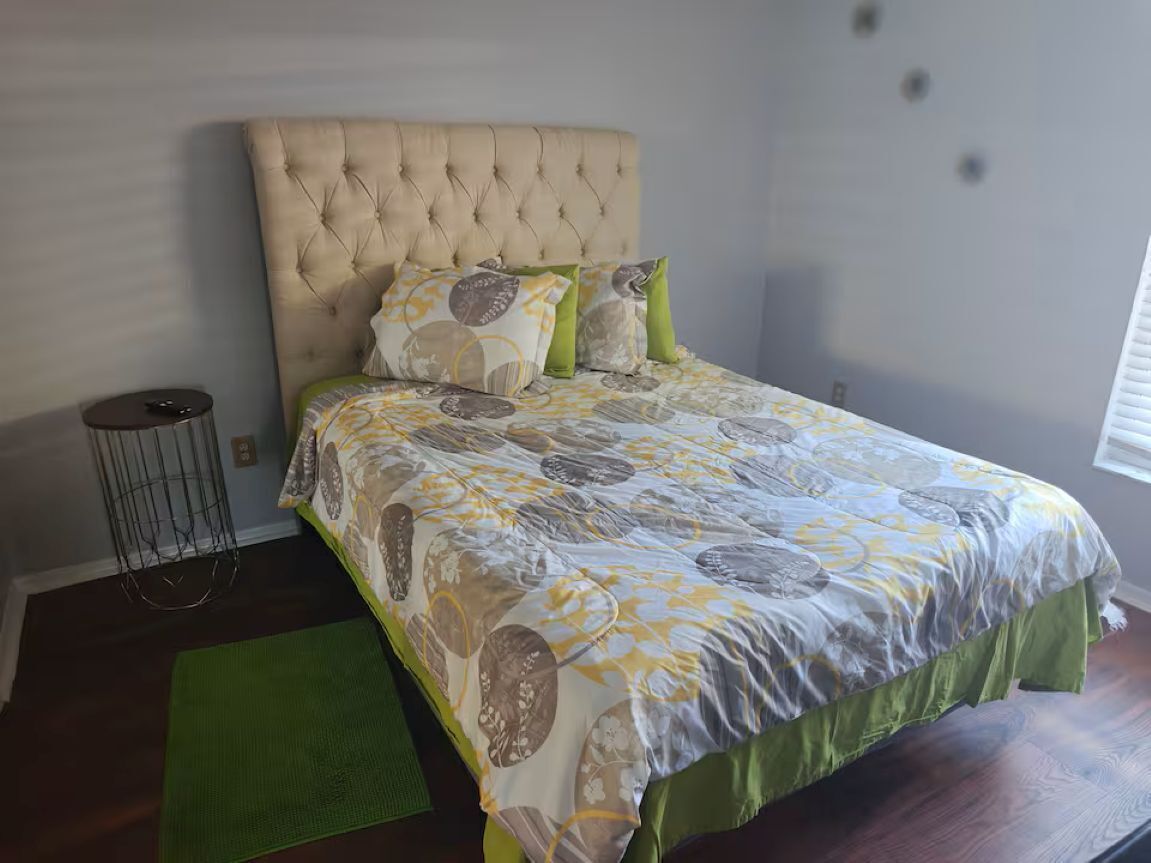 Un dormitorio con cabecera acolchada, colcha estampada y alfombra verde.