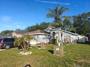 A residential house with a garage, a lawn with palm trees, and a parked car. - Tropical Pool Home Gazebo, Grill & Bar (Kissimmee)