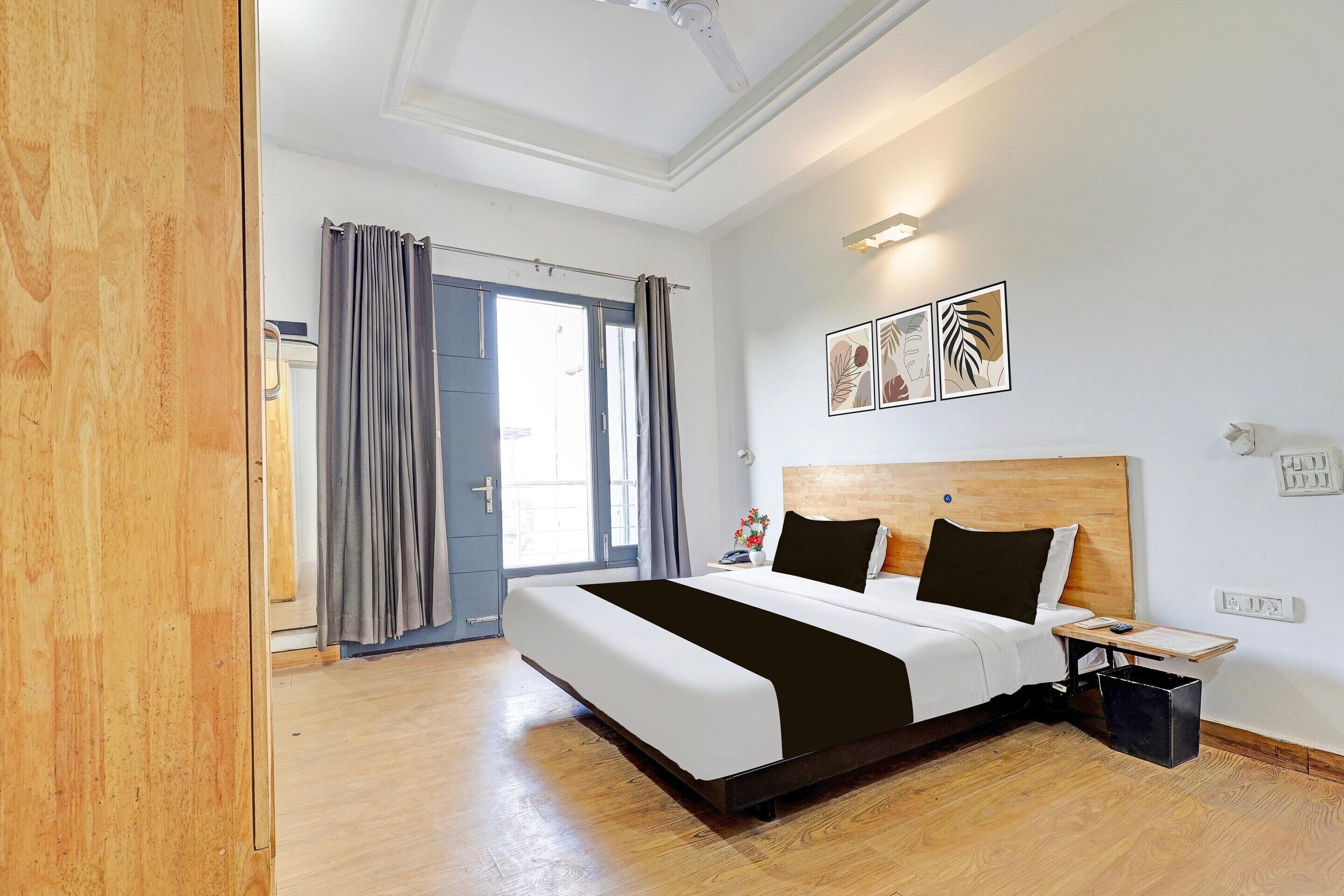 A hotel room with a large bed, a bedside table, a nightstand, a wall-mounted light, and a door with curtains.