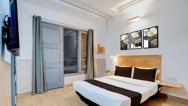 A bedroom with a bed, a TV, a sliding door, and artwork on the wall. - Deluxe Sector 49 Sohna Road (Gurugram)
