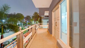 A balcony with a view of a street and palm trees, a railing, and a door with glass panels. - Deluxe Sector 49 Sohna Road (Gurugram)