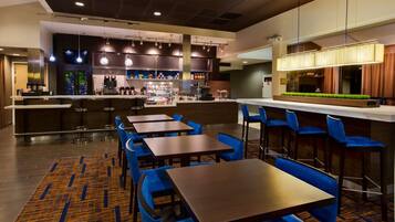 A modern bar area with multiple seating options, a counter with a beverage display, and a kitchen in the background.