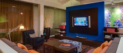A modern living room with a large flat-screen TV mounted on a blue accent wall, a comfortable sofa set, a coffee table, and a decorative plant.