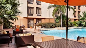 Zona junto a la piscina con mobiliario de mimbre, una mesa y un espacio de descanso cubierto.