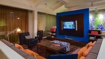 Una sala de estar moderna con un televisor de pantalla plana grande montado en una pared azul decorativa, un sofá cómodo, una mesa de centro y una planta ornamental.