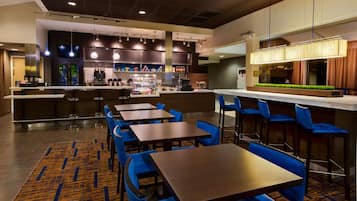 A modern bar area with multiple seating options, a counter with a beverage display, and a kitchen in the background.