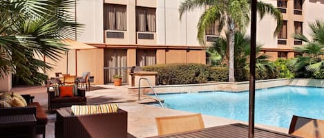 A poolside area with wicker furniture, a table, and a covered seating area.