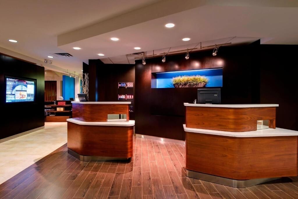 Un área de recepción con dos mostradores de madera, una pantalla digital y una planta en maceta.