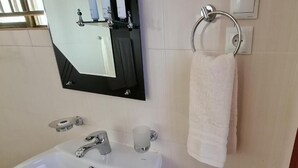 A bathroom with a sink, mirror, towel ring, and a toilet paper holder.