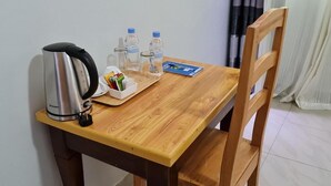 A wooden table with a kettle, water bottles, a tray with pens, and a card.