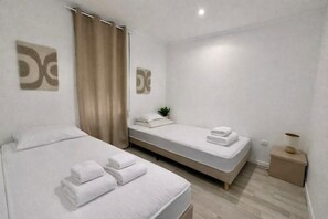 A hotel room with two beds, a small bedside table with a lamp, and a plant on the nightstand.