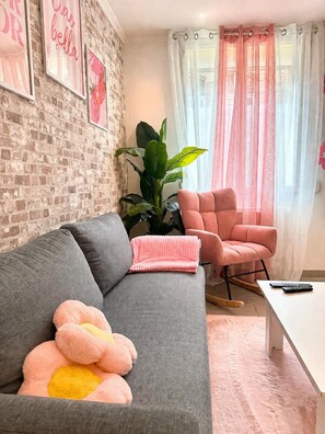 A living room with a grey sofa, a pink armchair, a large green plant, and a pink cushion.