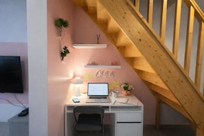 A room with a desk, a laptop, a smartphone, a lamp, a TV, and a staircase.