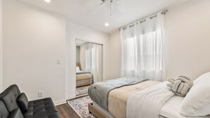 A bedroom with a bed, a black sofa, a ceiling fan, and a view of another room through a mirror.