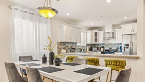 A modern kitchen with white cabinets, a central island, and a dining area with a white table and grey chairs.