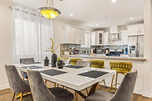 Una cocina moderna con armarios blancos, una isla central y una zona de comedor con una mesa blanca y sillas grises.
