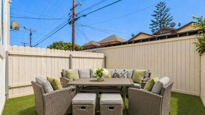 A patio with a dining table and wicker furniture, surrounded by a white fence.