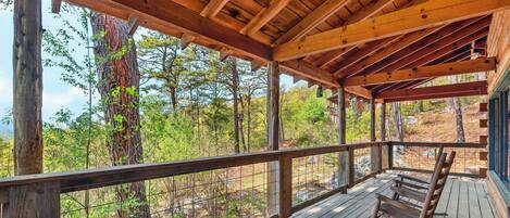 A wooden deck with a railing, overlooking a forested area.