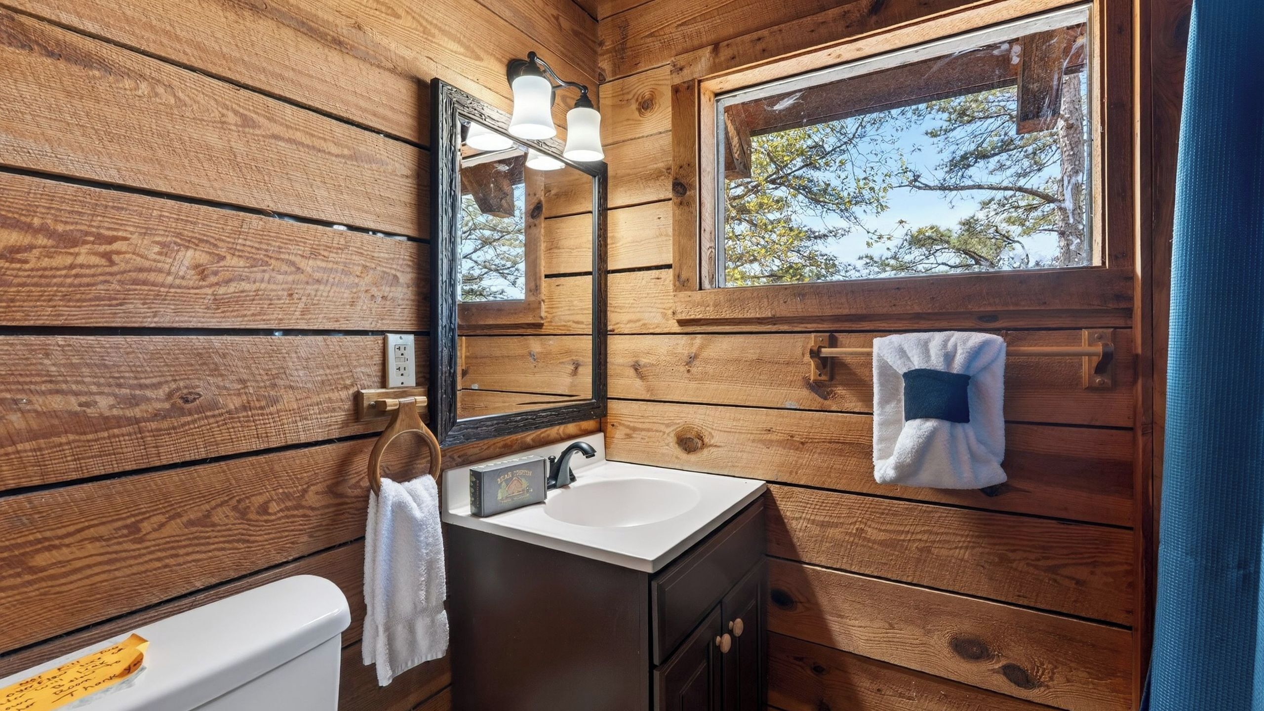 Bagno di una baita in legno con lavandino, specchio e finestra.