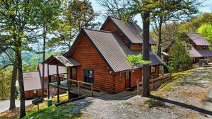A wooden cabin with a porch, surrounded by trees and a gravel path. - Sleeps 42, 7 Cabins Private Hot Tubs + Shared Fire Pit + Mountain Views + Covered Decks 7 Min to Townsend (Townsend)
