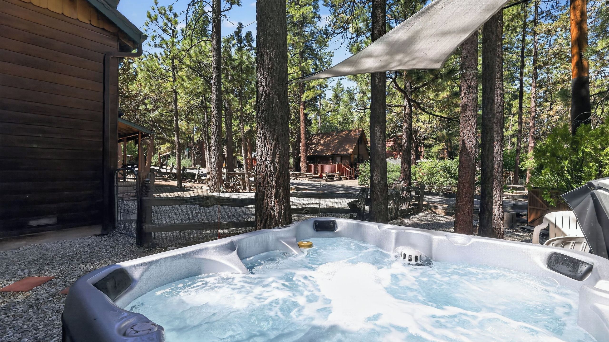 Un jacuzzi rodeado de árboles, una cabaña de madera y un área cubierta.